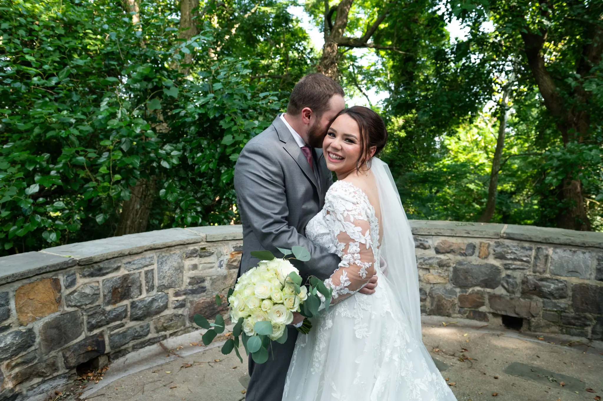 Photo of a groom and a bride holding a bouquet of white roses for outdoor wedding venues.