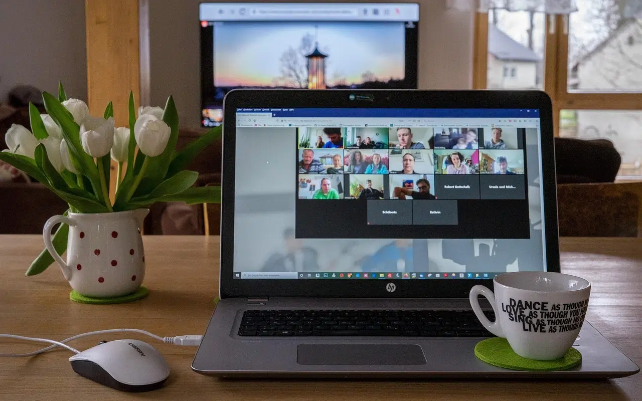 Photo of a video meeting on a laptop with a mug and a vase on the desk.