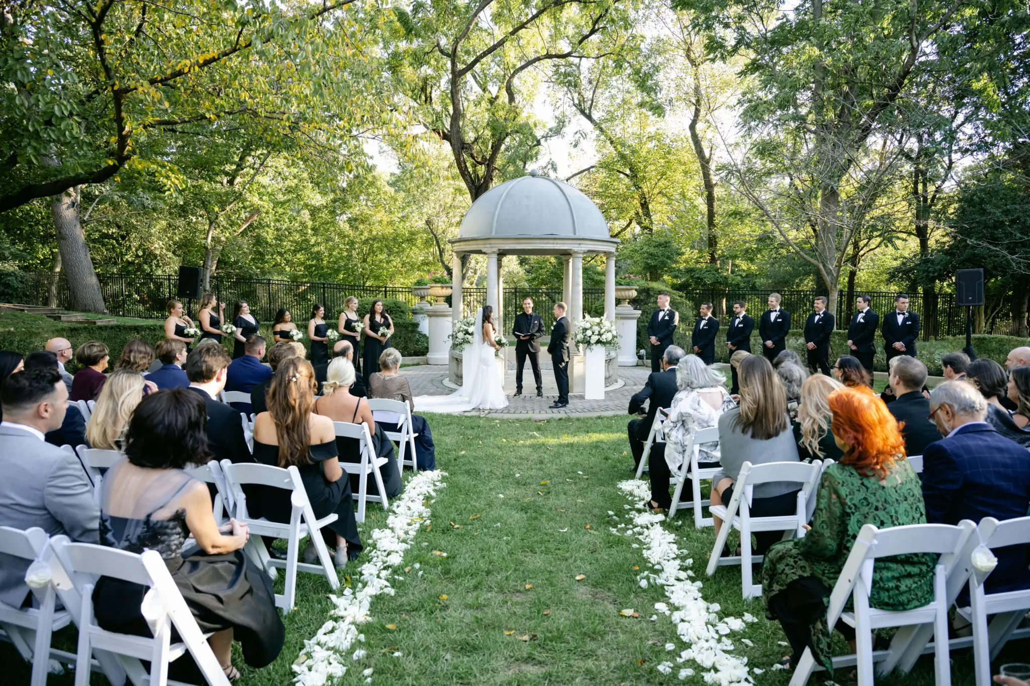 Photo of a wedding ceremony in a garden with seated guests and white flower decorations.