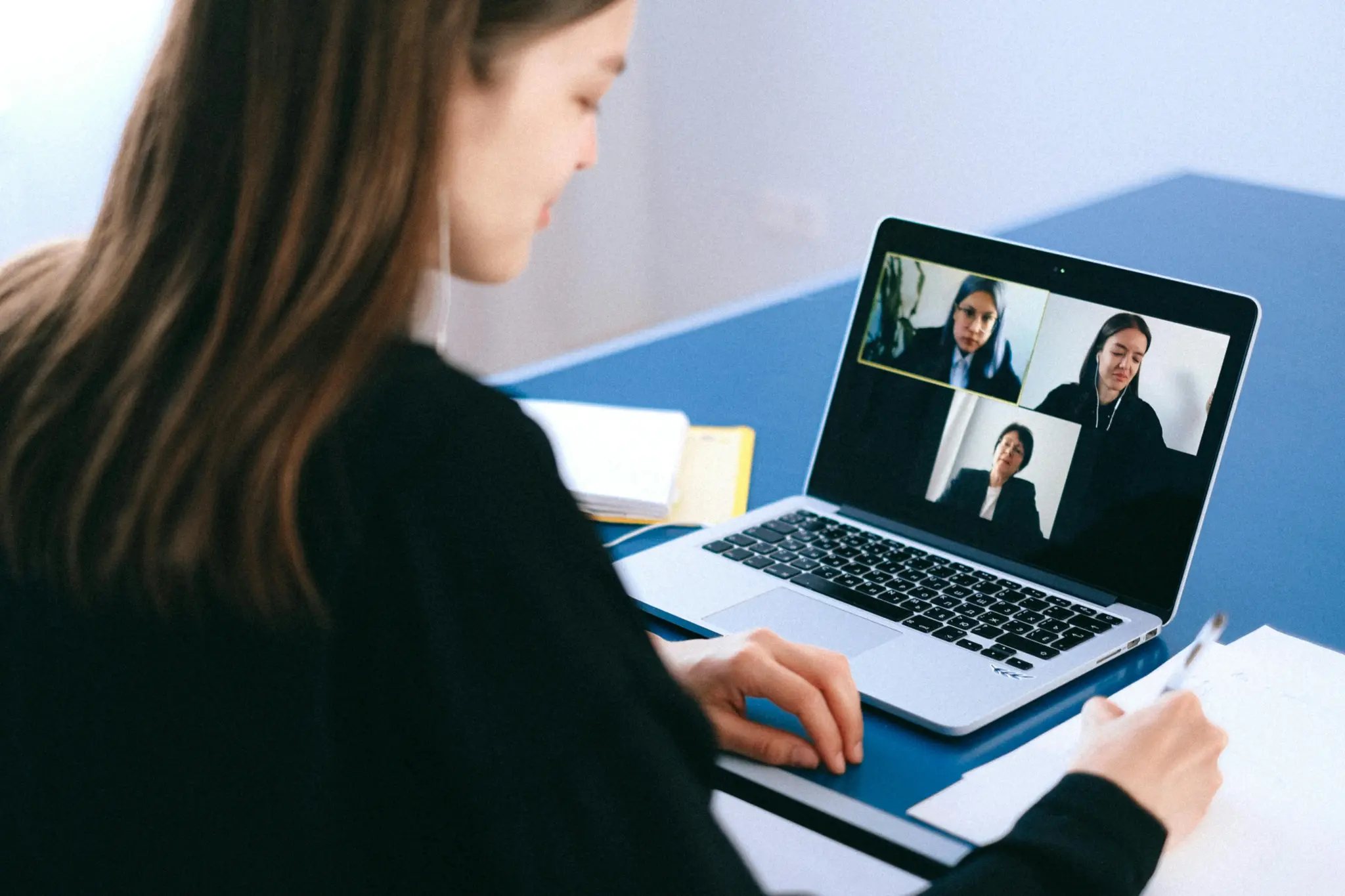 Photo of a woman in a virtual meeting with her laptop taking notes.