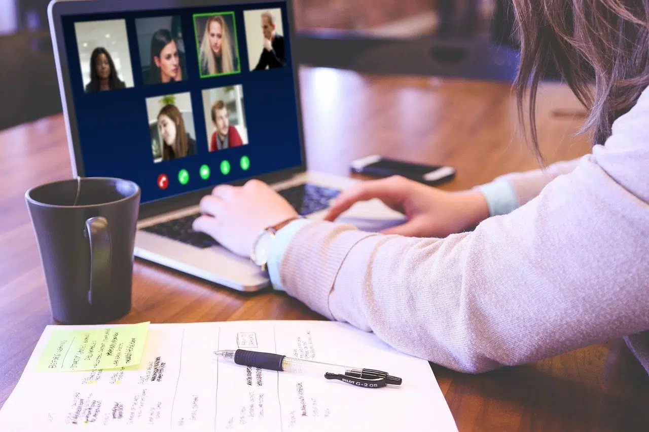 Photo of a woman in an online meeting on her laptop with notes on her desk.