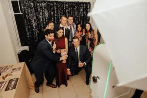Photo of wedding guests taking pictures at a photo booth with signs and a sparkly backdrop.
