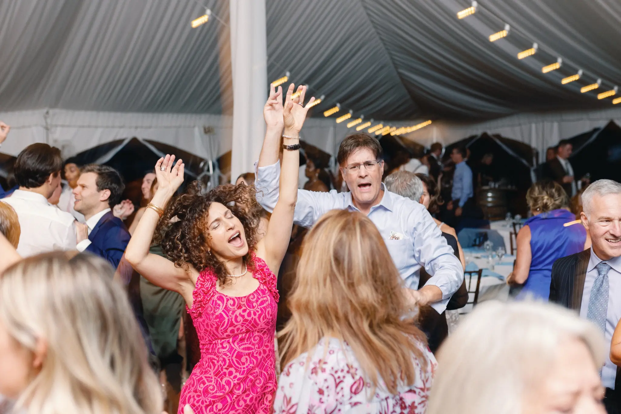 Photo of a woman in a pink dress and a man wearing a blue shirt dancing at a party among the attendees.