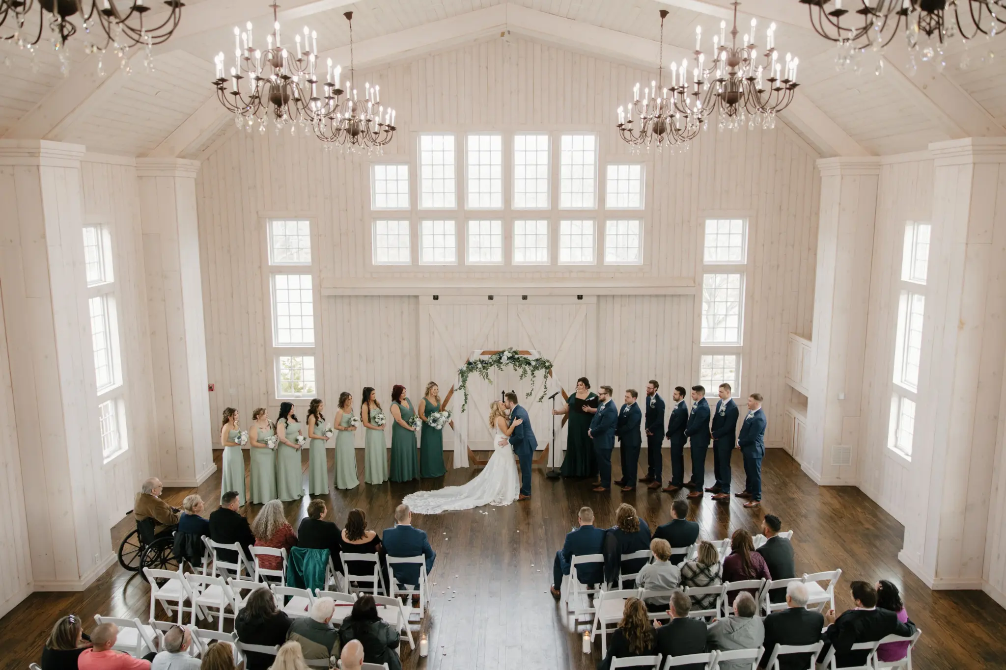 Photo of the bride and groom kissing surrounded by the bridesmaids and groomsmen while the guests are seated.