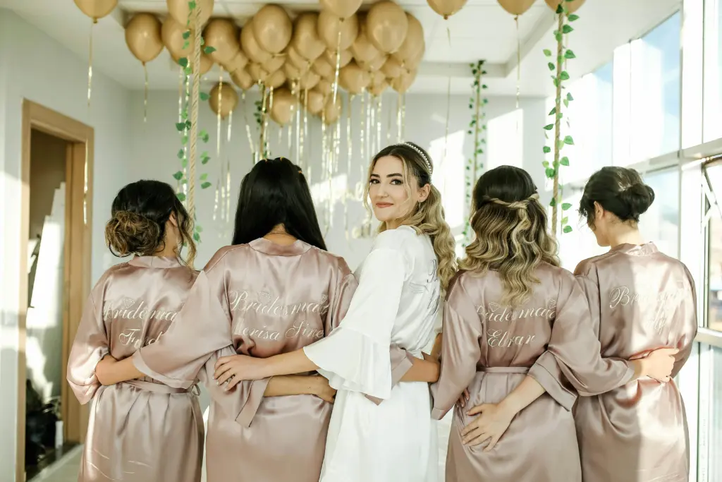 photo of a bride standing with her bridesmaids with their backs towards us with golden balloons and vines hanging from the ceiling