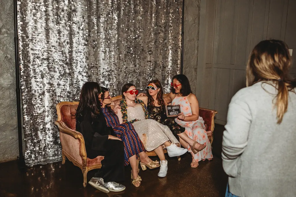 photo of women wearing fun glasses and holding signs while sitting on a couch with a backdrop