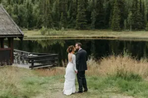 photo of a bride and groom kissing in a forest in front of a lake