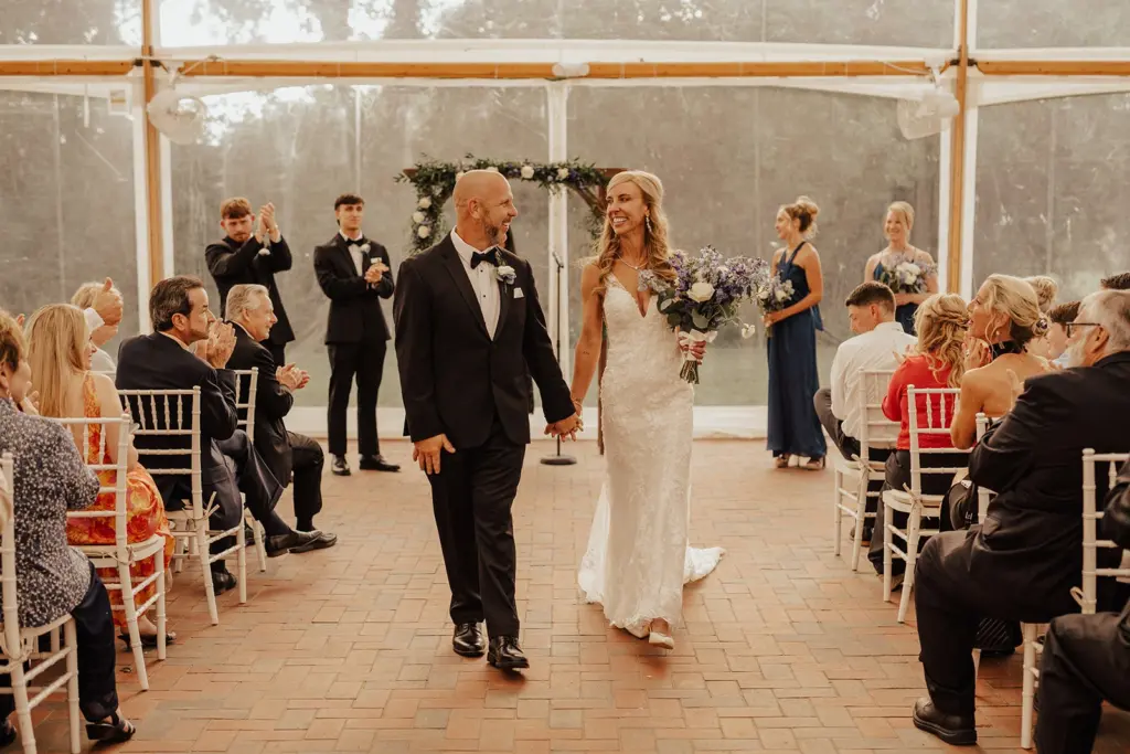 photo-of-a-couple-walking-down-the-aisle-while-the-bride-holds-a-purple-bouquet-for-how-much-does-a-venue-for-a-wedding-cost