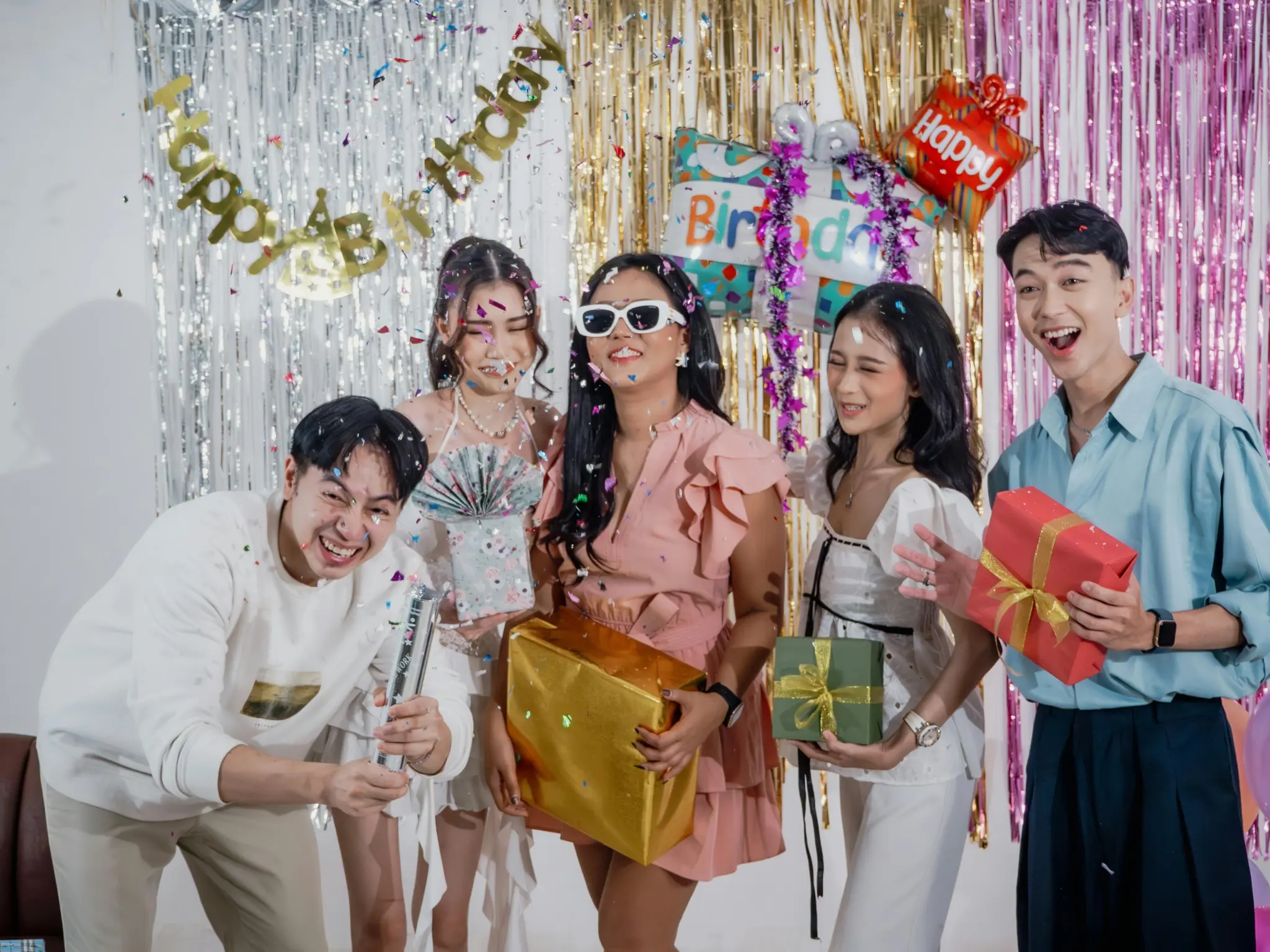 photo-of-a-group-of-teenagers-laughing-and-holding-presents-with-confetti-and-a-sparkly-backdrop