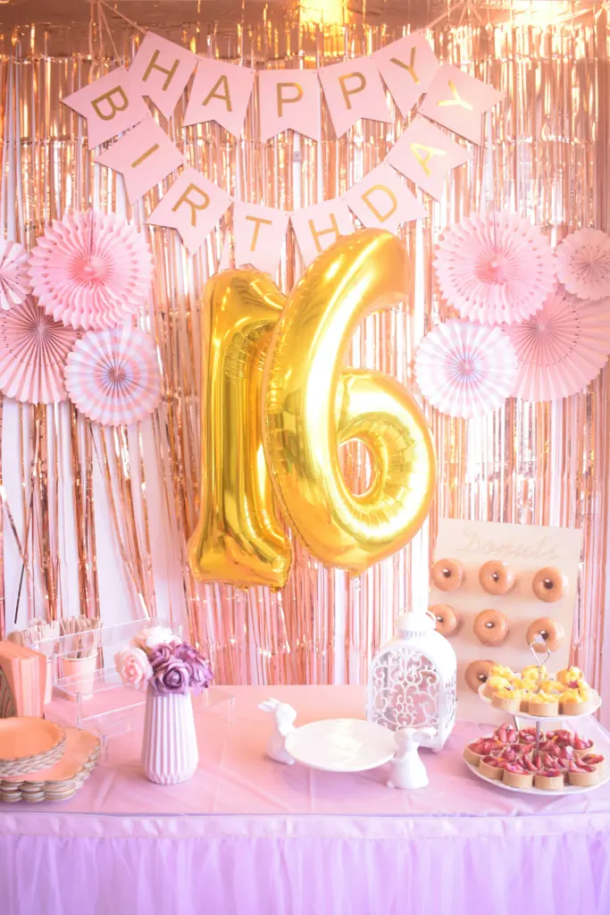 photo-of-a-pink-backdrop-with-a-happy-birthday-sign-golden-balloons-for-the-number-16-and-cupcakes-on-a-table