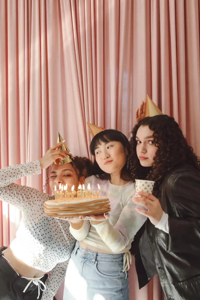 photo-of-three-girls-holding-up-a-birthday-cake-with-a-pink-backdrop-for-birthday-party-ideas-for-teenagers