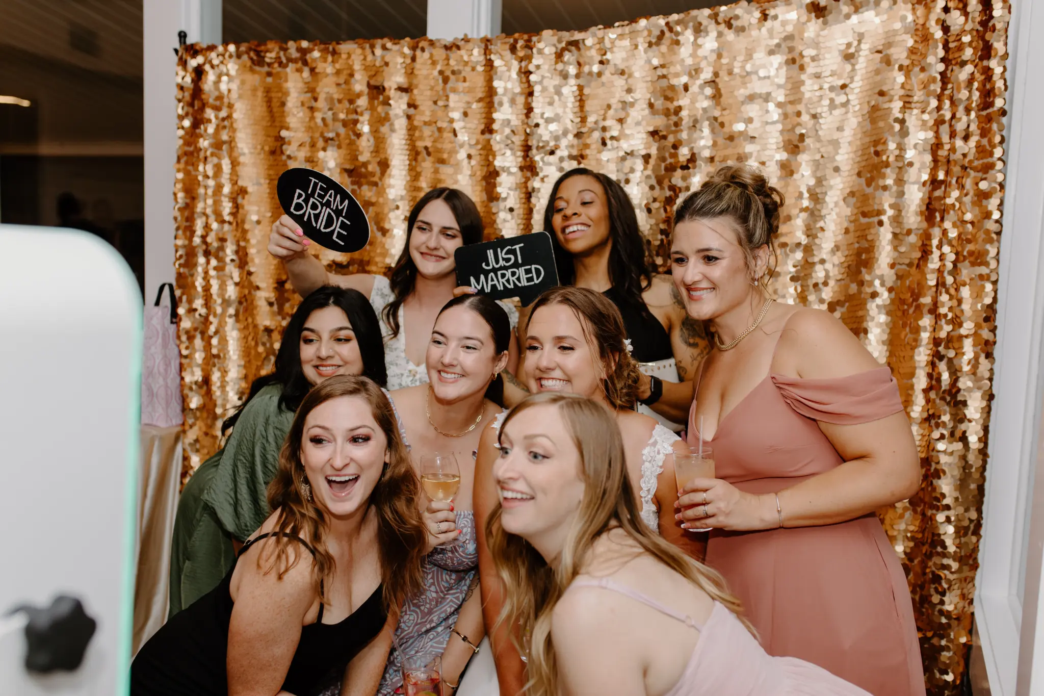 group of women smiling at wedding photo booth with gold backdrop signs