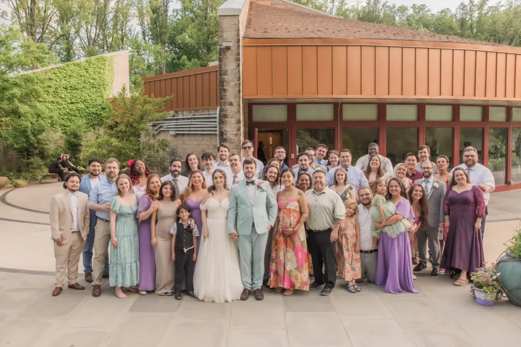 photo of a bride and groom posing for a picture with their family outside their wedding venue