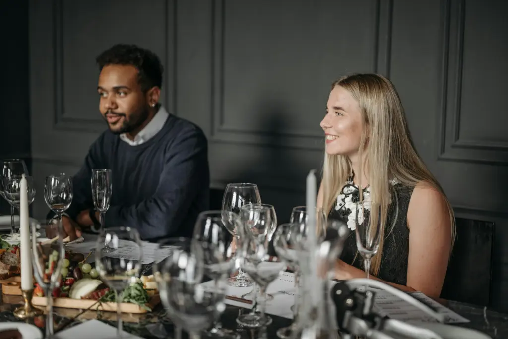 photo of a woman and a man seated at a dinner table filled with glasses and candles and a charcuterie board