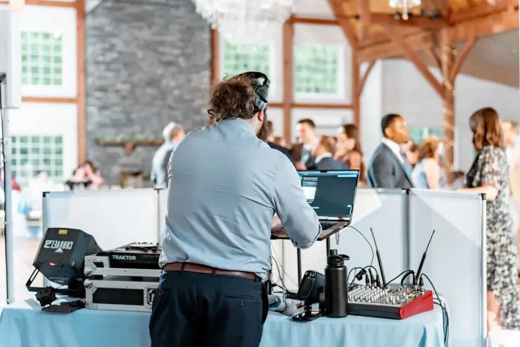 photo of a man working the dj at a party with headphones on and a laptop and dj equipment on the table