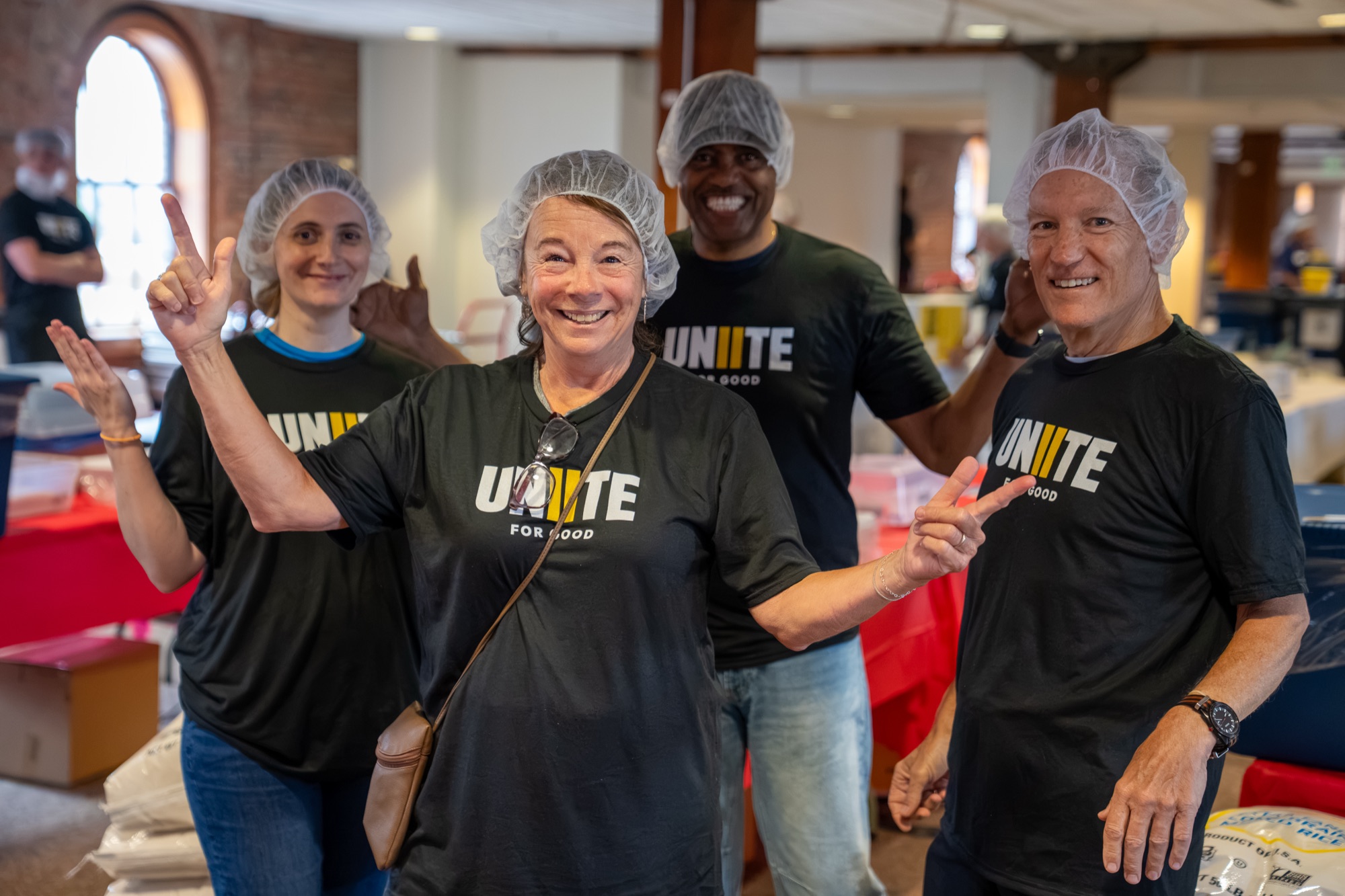 Volunteers in UNITE shirts smile and wave on the meal pack floor