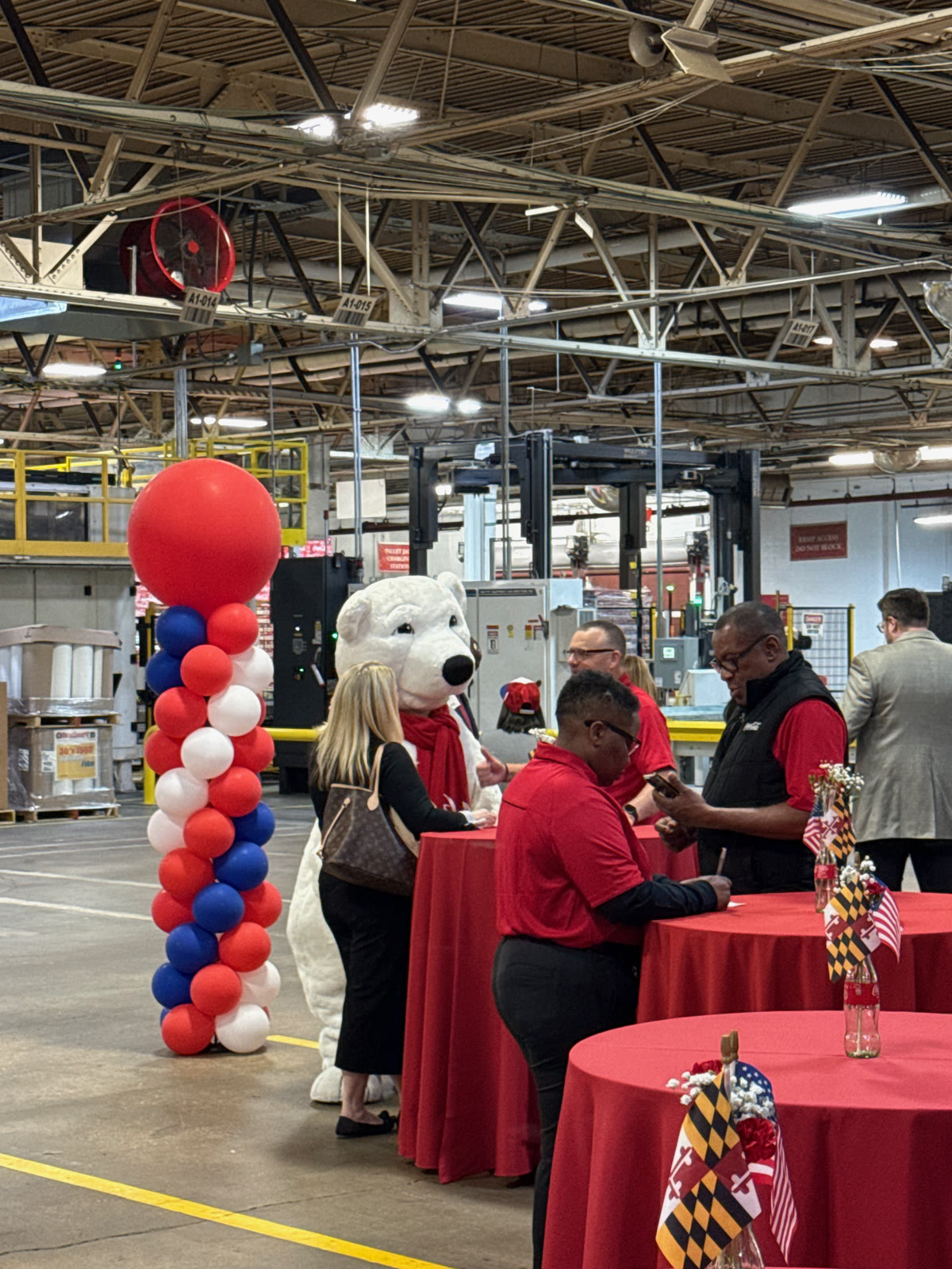 Guests at red high-top tables beside a red, white and blue balloon column and the Coca-Cola polar bear