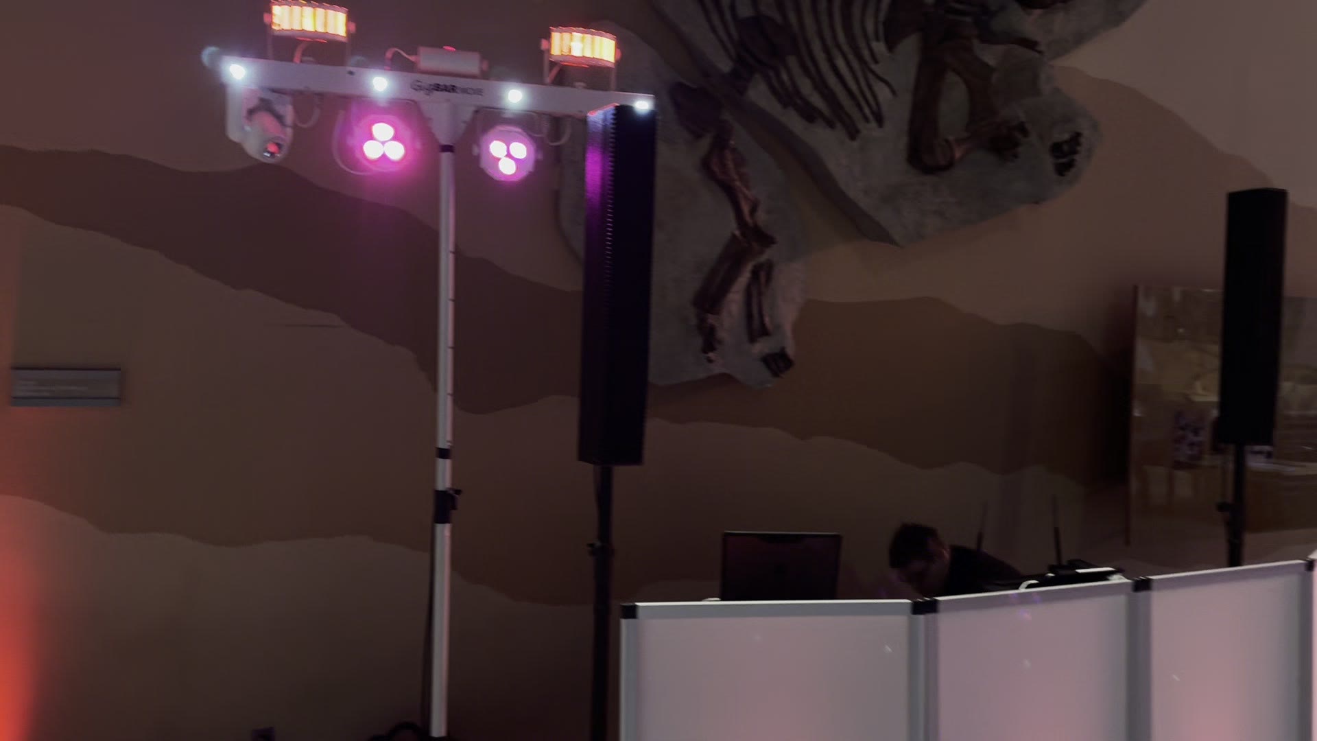 BSE DJ booth with a white facade and lighting rig beside a dinosaur skeleton